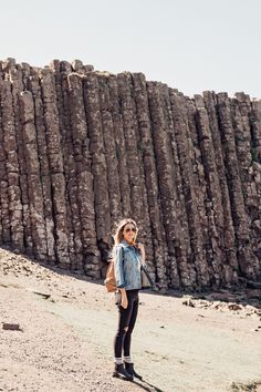 a woman standing on top of a dirt field next to a tall rock formation with rocks in the background