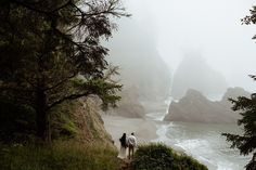 two people are walking down a path near the ocean on a foggy, overcast day