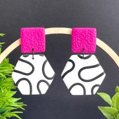 pair of pink and white earrings hanging from wooden hoop with green plant in the background