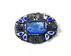 Lovely brooch with deep blue colors. Designed with blue enamel guilloche leaves and small glass accents. Small amount of wear in pin backing. On the first picture top right there is a small amount of wear to the blue of the enamel but the white is still intact. Great working clasp. Good vintage condition with very little wear. Center stone is open work and prong set where the chaton accents on the sides are bevel set into the piece. This line was designed by Neiger Brothers and showcases the uni Formal Blue Cabochon Brooch, Blue Cabochon Brooch For Formal Occasions, Formal Blue Enamel Brooches, Blue Cabochon Brooches For Wedding, Antique Blue Collectible Brooches, Ornate Blue Brooch For Formal Occasions, Ornate Blue Wedding Brooches, Ornate Blue Brooches For Wedding, Antique Blue Enamel Brooches