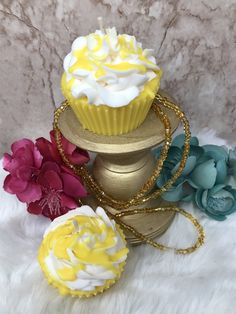 two cupcakes with white frosting and yellow icing on a gold stand