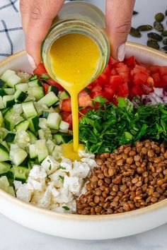 someone pouring dressing into a bowl filled with vegetables and nuts, including cucumbers