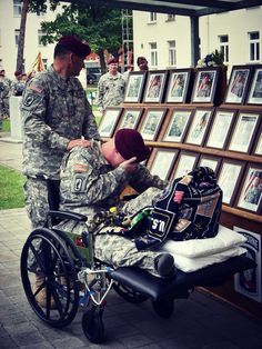 two soldiers standing next to a man in a wheel chair with pictures on the wall behind him