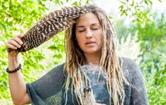 a woman with long dreadlocks holding a bird in her hand and looking at it