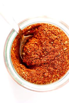 a glass bowl filled with red seasoning on top of a white countertop next to a wooden spoon