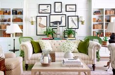 a living room filled with white furniture and lots of pictures on the wall above it