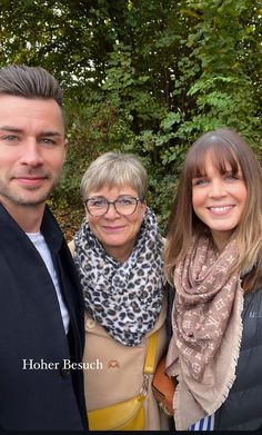 three people standing next to each other in front of trees