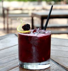 a drink with blackberries and lemon wedges on the rim sitting on a wooden table