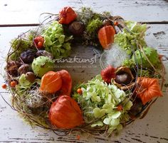 an arrangement of flowers and leaves in a wreath on a wooden surface with the word autumn written below it