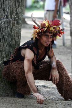 a man dressed up as a deer with horns and leaves on his head sitting next to a tree