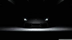 a black sports car in the dark with its headlights turned on and it is glowing