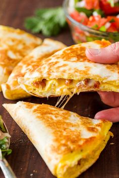 a person is holding up a piece of quesadilla on a cutting board