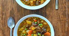 two bowls of stew with carrots, peas and potatoes on a wooden table top