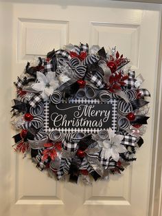 a christmas wreath on the front door decorated with black and white ribbon, red and silver poinsettis