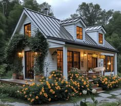 a white house with lots of windows and yellow flowers in the front yard, surrounded by greenery