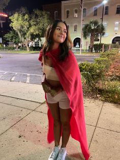 a woman standing on the sidewalk wearing a red cape