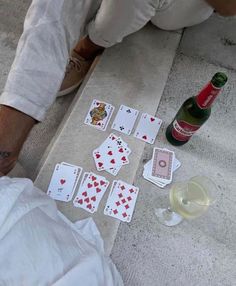 a man sitting on the ground next to playing cards and a bottle of wine,