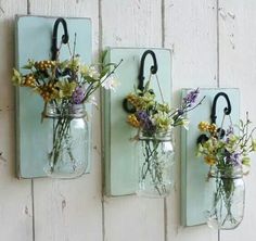 three mason jars with flowers in them are hanging on the wall next to each other