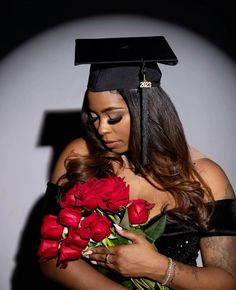 a woman wearing a graduation cap and gown holding red roses in her hands while looking at the camera