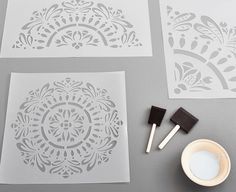 four stencils are laid out on a table next to a cup and brush