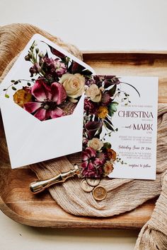 wedding stationery with floral bouquets and gold key on wooden tray next to white envelope