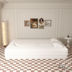 a white bed sitting on top of a checkered floor next to a wall with pictures above it