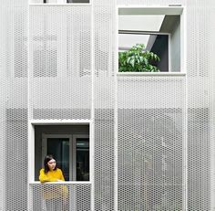 a woman is looking out the window of a white building with perfored walls