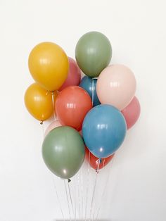 a bunch of balloons floating in the air on top of a white wall with string