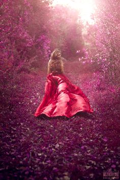 a woman in a red dress is walking through the woods with purple flowers on her head