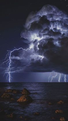 lightning strikes over the ocean on a cloudy night with rocks in foreground and dark clouds above