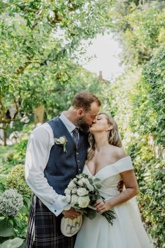 a bride and groom kissing in front of greenery on their wedding day at the park