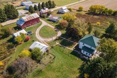 an aerial view of a farm with several buildings and trees in the background, including two red barns