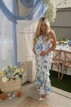 the pregnant woman is posing in her blue and white floral print dress, while standing next to a baby carriage