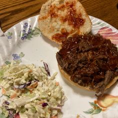 a plate topped with a sandwich and coleslaw next to a bun covered in barbecue sauce