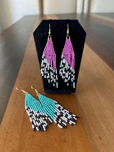 two pairs of beaded earrings sitting on top of a wooden table next to a black stand