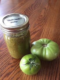 two green tomatoes sitting on top of a wooden table next to a jar of pesto