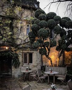 an outdoor dining area with wooden chairs and tables in front of a stone building at night