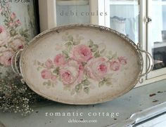 a white tray with pink roses painted on it sitting on top of a table next to a window