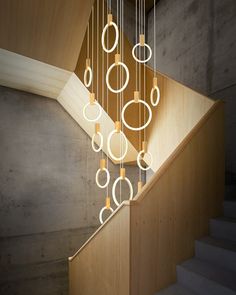 an artistic light fixture hanging from the ceiling in a stairwell with wooden steps and handrails