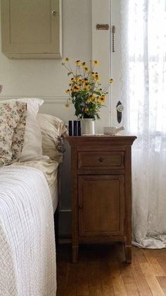 a bedroom with a bed, nightstand and flowers on the table in front of it