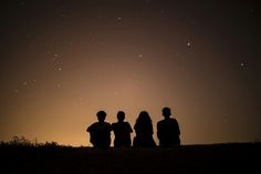 three people standing on top of a hill under a night sky with stars in the background