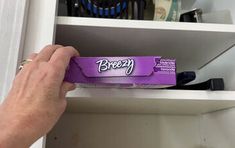 a person is holding a purple box in front of a white shelf with other items on it