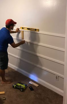 a man in blue shirt and red hat working on white paneled wall with tools