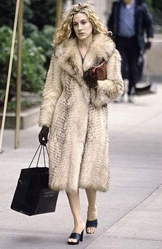 a woman is walking down the street with her hand in her pocket and wearing a fur coat