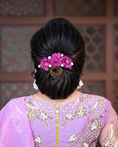 the back of a woman's head with pink flowers in her hair, wearing a purple sari