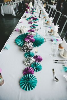 a long table is set up with paper fans and napkins on the runner line