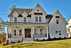 a white two story house with black roof and front porch on a sunny day in the country