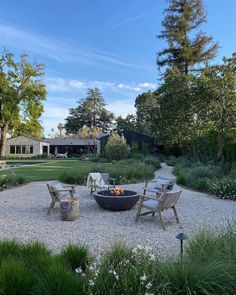 an outdoor fire pit in the middle of a gravel area surrounded by trees and bushes