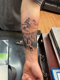 a man's arm with a mountain and deer tattoo on it