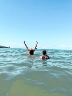 two people are swimming in the ocean with their arms up and hands raised to the sky